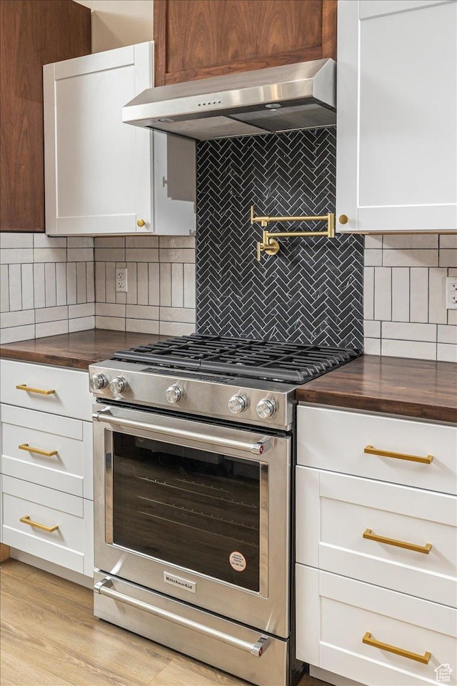kitchen featuring white cabinets, wall chimney exhaust hood, stainless steel stove, and tasteful backsplash