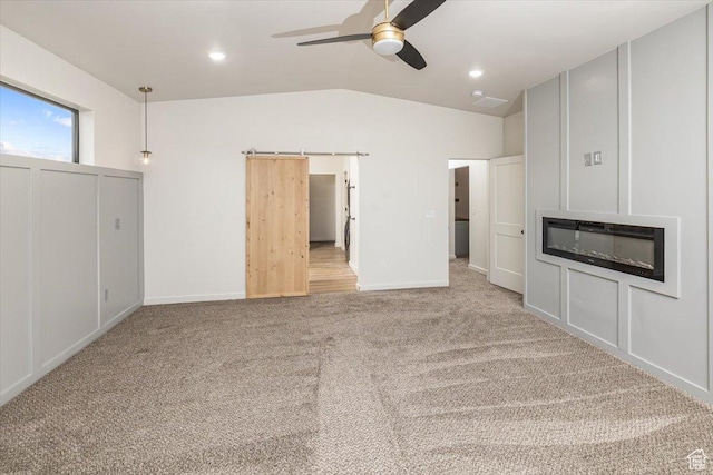unfurnished living room with a barn door, light colored carpet, vaulted ceiling, and ceiling fan