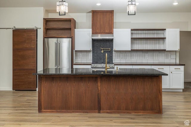 kitchen featuring pendant lighting, high end fridge, white cabinetry, and a kitchen island with sink