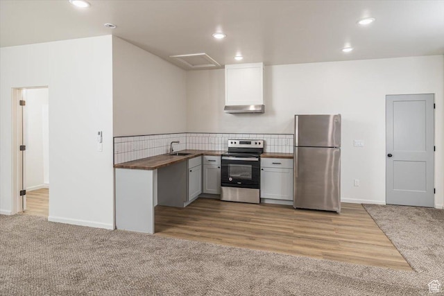 kitchen with sink, wall chimney exhaust hood, wood counters, light carpet, and appliances with stainless steel finishes