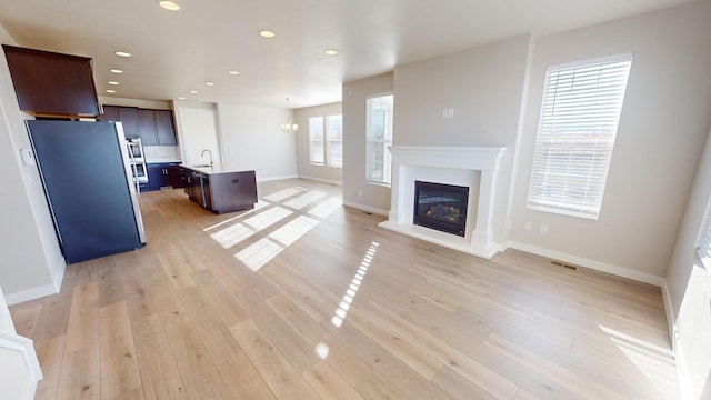 633 W Junegrass Ln, Stansbury Park, UT 84074 - unfurnished living room featuring light wood-type flooring, sink, and an inviting chandelier