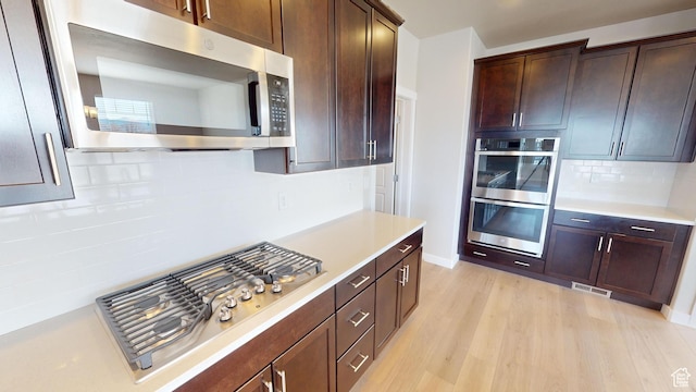 633 W Junegrass Ln, Stansbury Park, UT 84074 - kitchen with decorative backsplash, light wood-type flooring, stainless steel appliances, and dark brown cabinetry