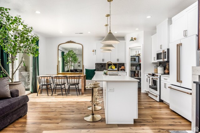 kitchen featuring sink, a kitchen island with sink, hanging light fixtures, white appliances, and decorative backsplash