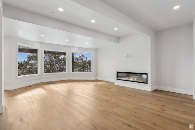 3097 E Corral Peak Cir Unit 145, Heber City, UT 84032 - unfurnished living room featuring light wood-style flooring, plenty of natural light, a glass covered fireplace, and baseboards