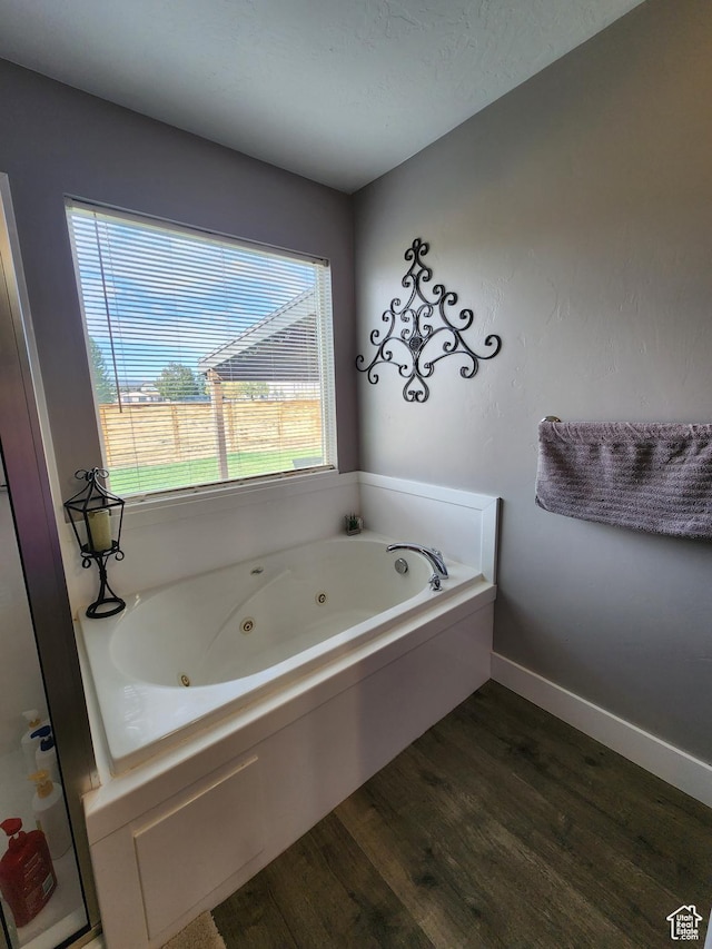 bathroom featuring a healthy amount of sunlight, wood-type flooring, and a tub