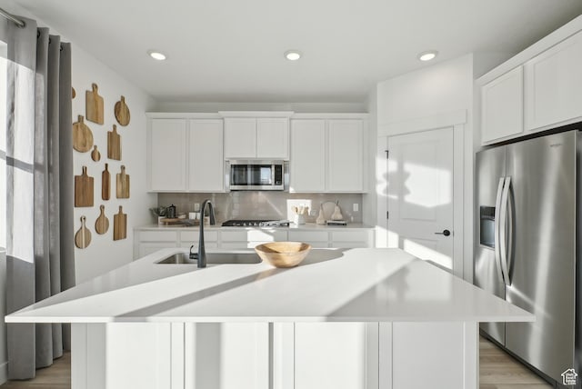 kitchen featuring a kitchen island with sink, light countertops, a sink, stainless steel appliances, and decorative backsplash