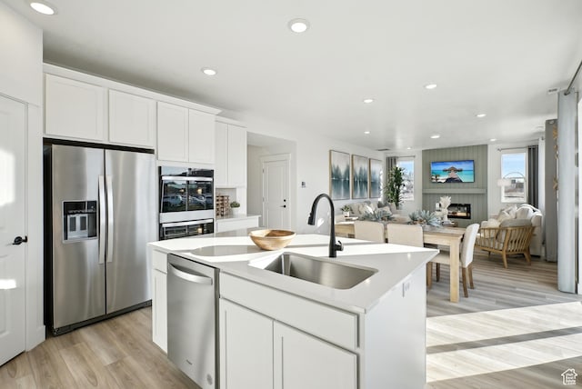 kitchen with a kitchen island with sink, a sink, stainless steel appliances, open floor plan, and light wood finished floors
