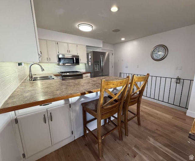 kitchen with kitchen peninsula, stainless steel appliances, sink, white cabinets, and hardwood / wood-style floors