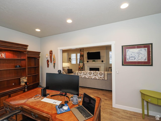 office area with baseboards, light wood-type flooring, recessed lighting, and a fireplace