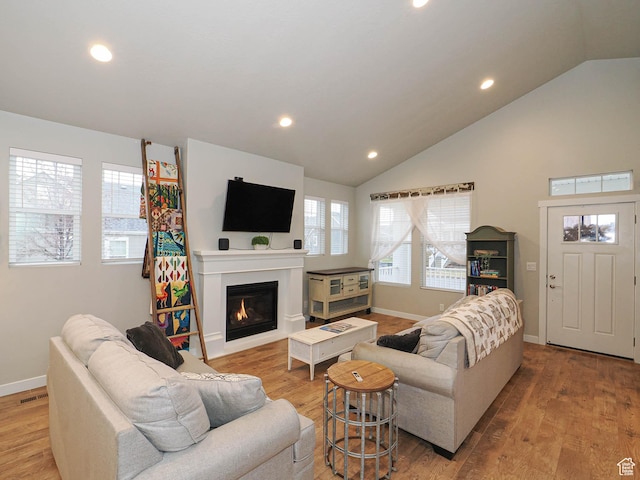 living room with baseboards, recessed lighting, vaulted ceiling, light wood-style flooring, and a glass covered fireplace