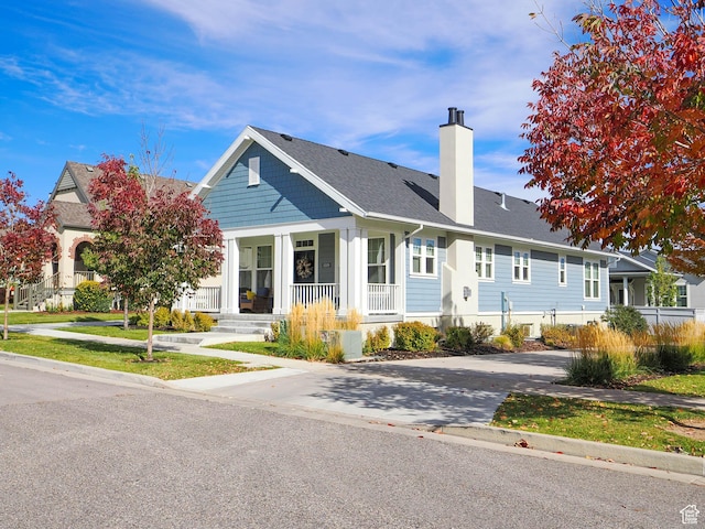 view of front of property with a porch, roof with shingles, a chimney, and concrete driveway