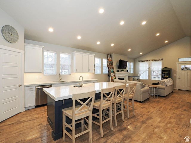kitchen featuring an island with sink, a fireplace, dishwasher, a sink, and light wood finished floors