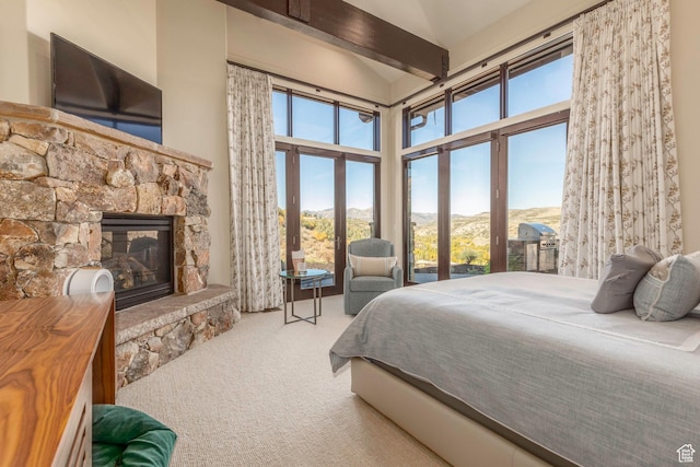 bedroom with a mountain view, multiple windows, a stone fireplace, and carpet