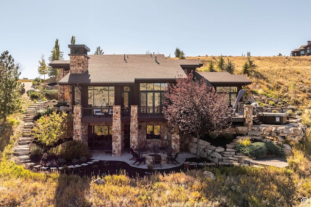 back of house featuring a patio, a chimney, and a shingled roof