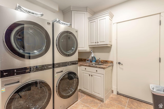 laundry room featuring cabinet space, stacked washing maching and dryer, and a sink