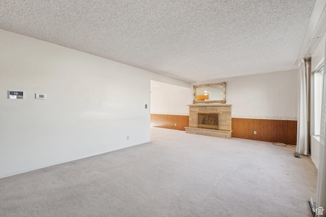 unfurnished living room featuring light carpet, a textured ceiling, a stone fireplace, and wooden walls