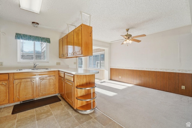 kitchen featuring kitchen peninsula, light colored carpet, ceiling fan, wooden walls, and sink