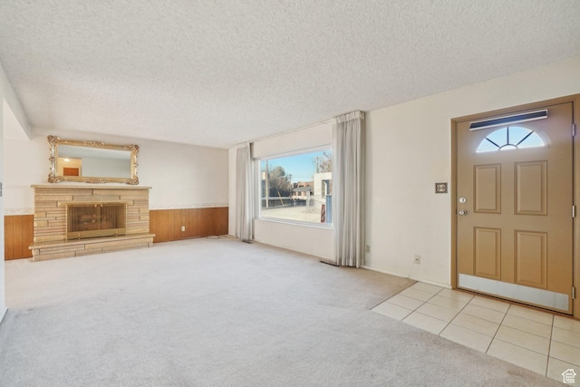 unfurnished living room with a healthy amount of sunlight, light colored carpet, a fireplace, and wooden walls