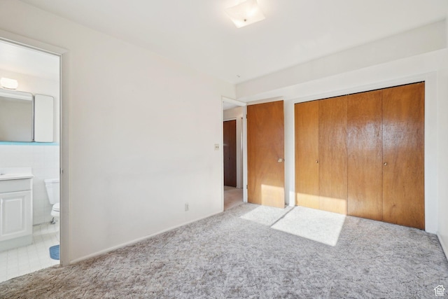 unfurnished bedroom featuring ensuite bath, light carpet, and a closet