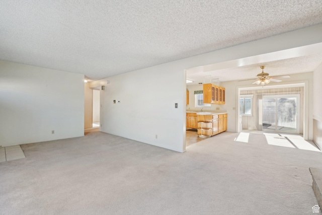 unfurnished living room with a textured ceiling, ceiling fan, sink, and light carpet