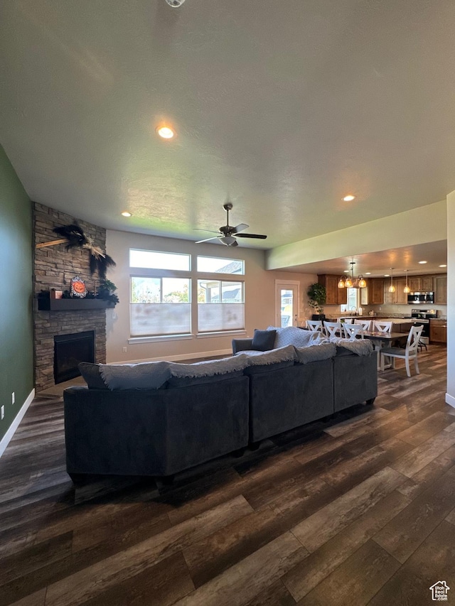 living room featuring a fireplace, dark wood-type flooring, and ceiling fan with notable chandelier