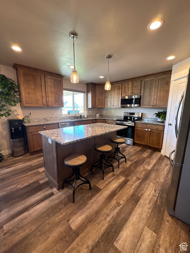 kitchen with light stone countertops, appliances with stainless steel finishes, decorative light fixtures, a kitchen island, and a breakfast bar area