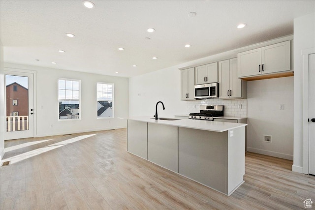 7029 W S Jordan Pkwy Unit 380, South Jordan, UT 84009 - kitchen featuring stainless steel appliances, light wood finished floors, decorative backsplash, a center island with sink, and light countertops