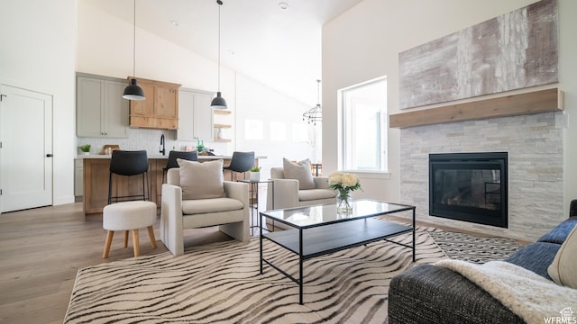 living room with light wood-type flooring, a glass covered fireplace, and high vaulted ceiling