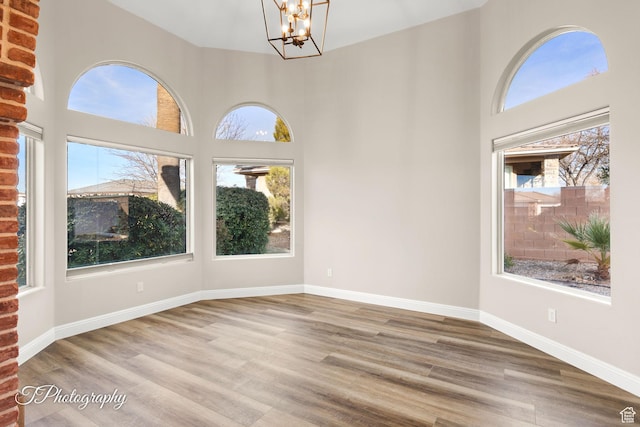 empty room featuring a towering ceiling, light wood-type flooring, and a notable chandelier