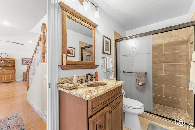 full bath featuring toilet, tiled shower, vanity, and wood finished floors