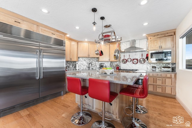 kitchen featuring light brown cabinets, a sink, wall chimney range hood, appliances with stainless steel finishes, and light wood-style flooring