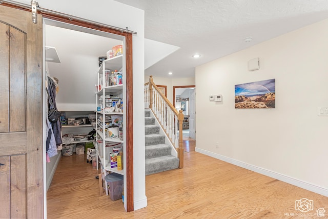 stairs featuring wood finished floors, recessed lighting, baseboards, and a barn door