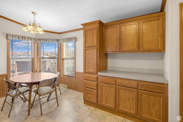 kitchen with a chandelier, pendant lighting, ornamental molding, and wood walls