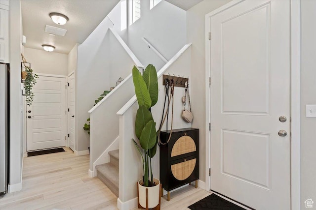 entryway featuring visible vents, baseboards, light wood-style flooring, and stairs