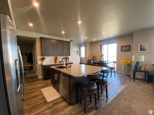 kitchen with dark wood-type flooring, sink, an island with sink, dark brown cabinetry, and stainless steel appliances