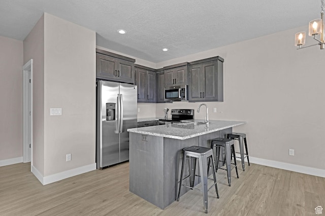 kitchen featuring sink, kitchen peninsula, a textured ceiling, a breakfast bar area, and appliances with stainless steel finishes