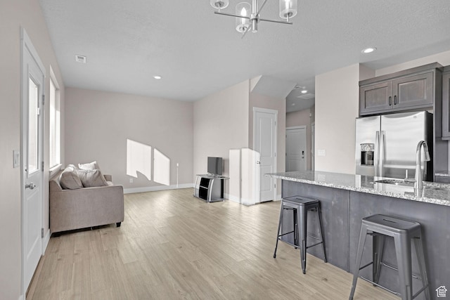 kitchen featuring a kitchen bar, stainless steel fridge, light stone counters, dark brown cabinets, and sink