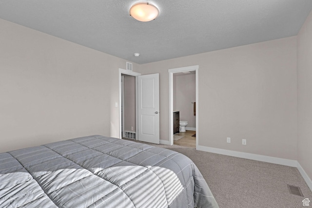 carpeted bedroom featuring a textured ceiling and ensuite bath
