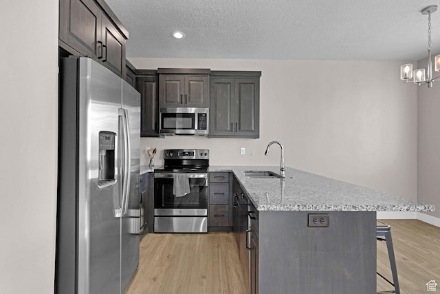 kitchen featuring a kitchen bar, a textured ceiling, stainless steel appliances, sink, and an inviting chandelier