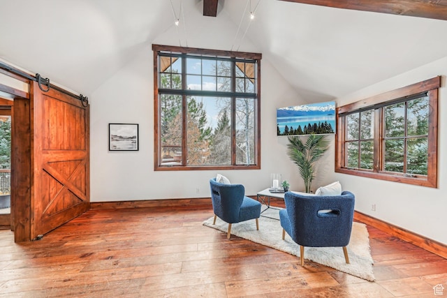 sitting room with a barn door, light hardwood / wood-style floors, and lofted ceiling