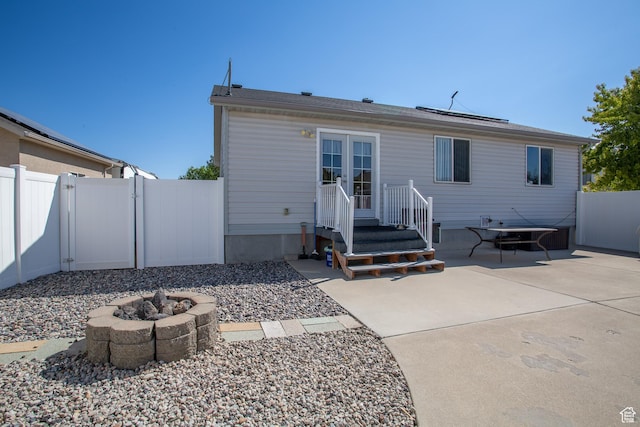rear view of property with french doors, fence, roof mounted solar panels, a patio, and a fire pit