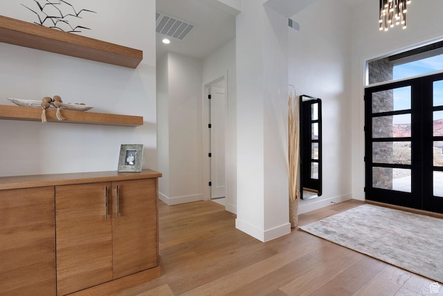 entryway with french doors, light wood-type flooring, and a notable chandelier