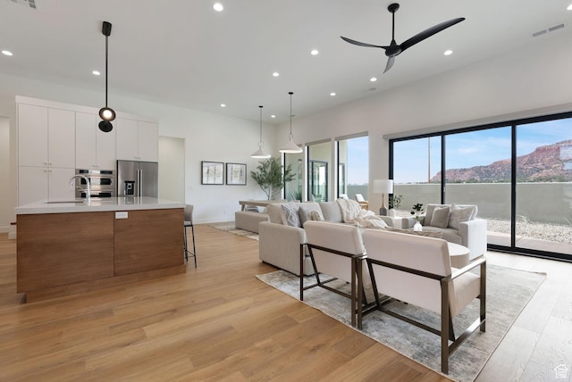 living room with ceiling fan, sink, a mountain view, and light wood-type flooring