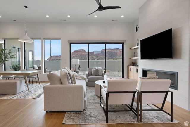 living room featuring built in shelves, ceiling fan, a fireplace, and light hardwood / wood-style floors