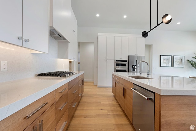kitchen featuring white cabinetry, sink, an island with sink, decorative light fixtures, and appliances with stainless steel finishes