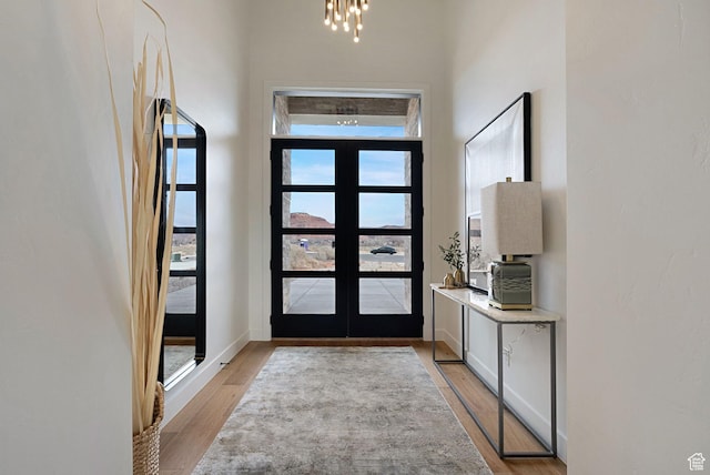 entrance foyer with french doors, light hardwood / wood-style flooring, and a notable chandelier