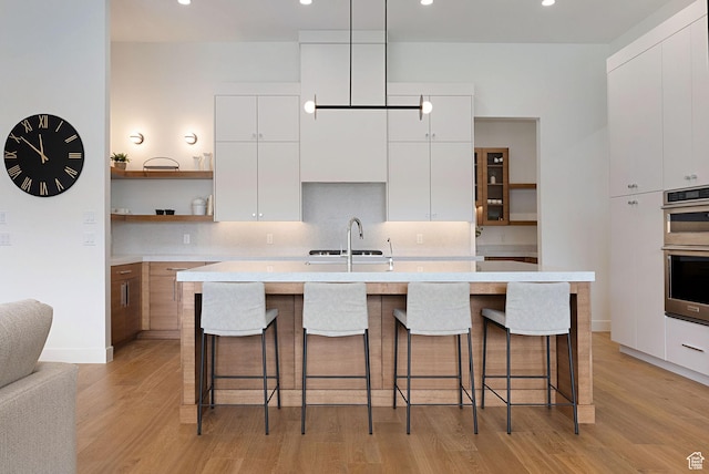 kitchen featuring white cabinets, a center island with sink, and stainless steel double oven