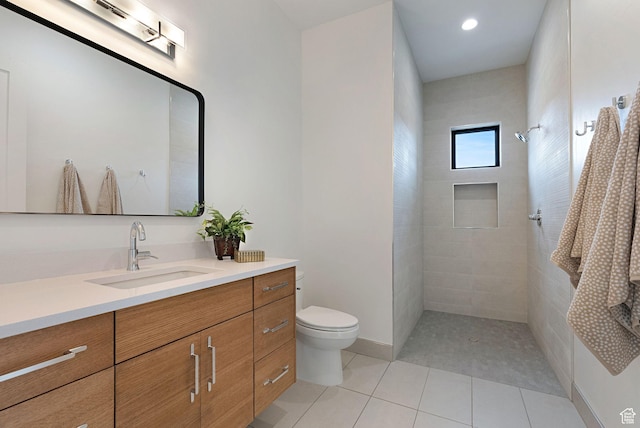 bathroom with tile patterned floors, vanity, tiled shower, and toilet
