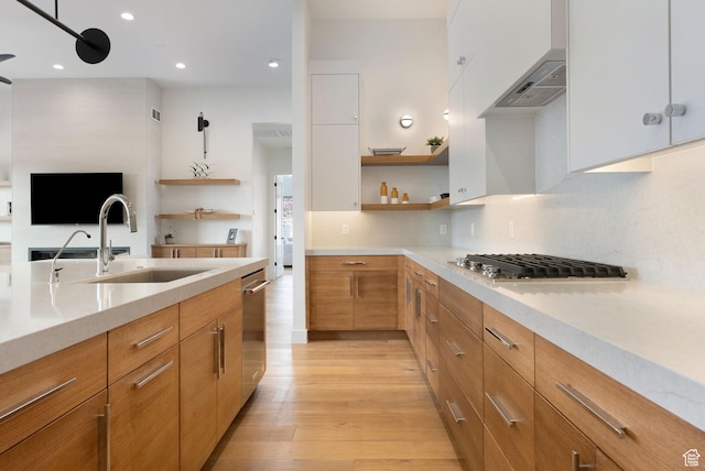 kitchen with appliances with stainless steel finishes, wall chimney range hood, sink, light hardwood / wood-style flooring, and white cabinetry