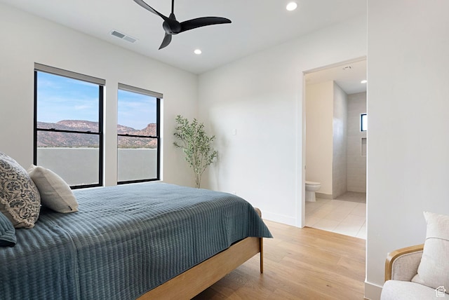 bedroom featuring ceiling fan, light hardwood / wood-style floors, a mountain view, and connected bathroom